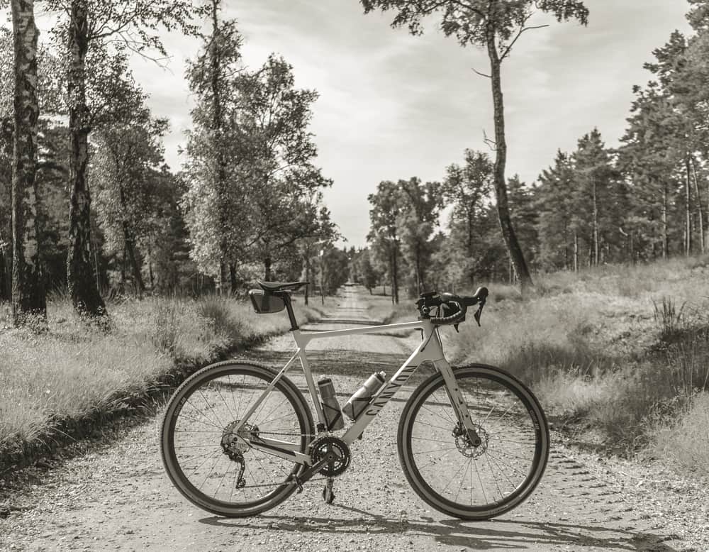 A gravel bike leaning against a field gate on a dirt track