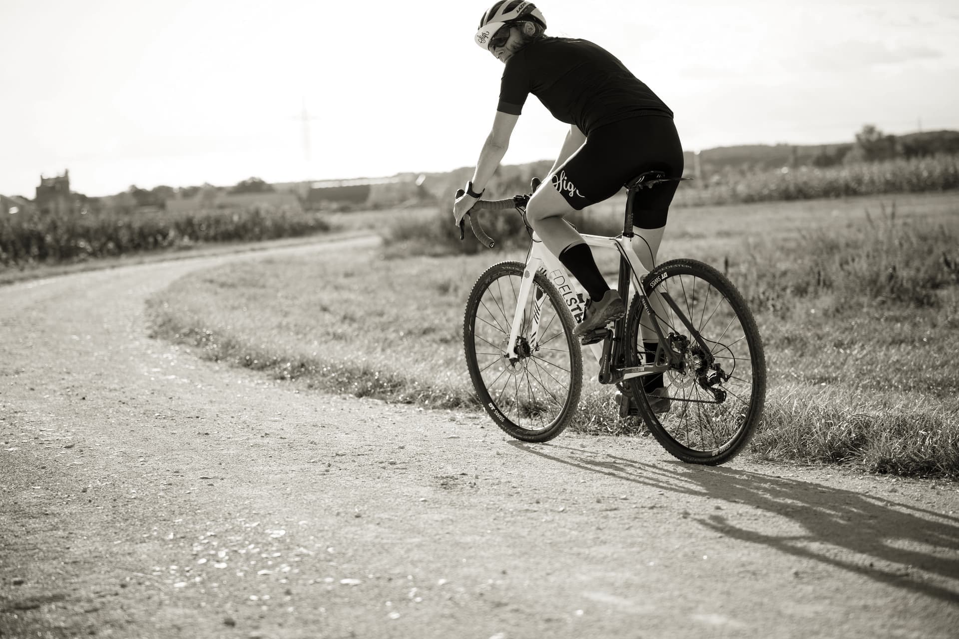 A rider on a gravel road running between open fields under flat light