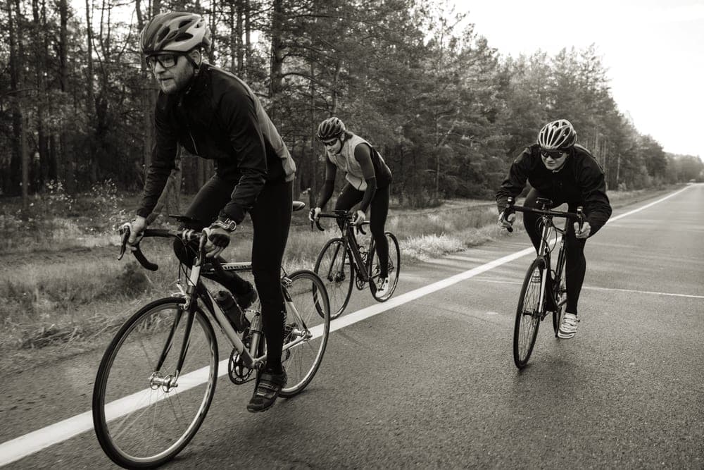 Three riders on road bikes on a quiet forest road